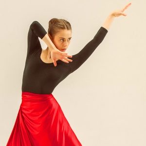Bailarina de danza española realizando una expresión intensa en una competición de flamenco, con vestido rojo y castañuelas.